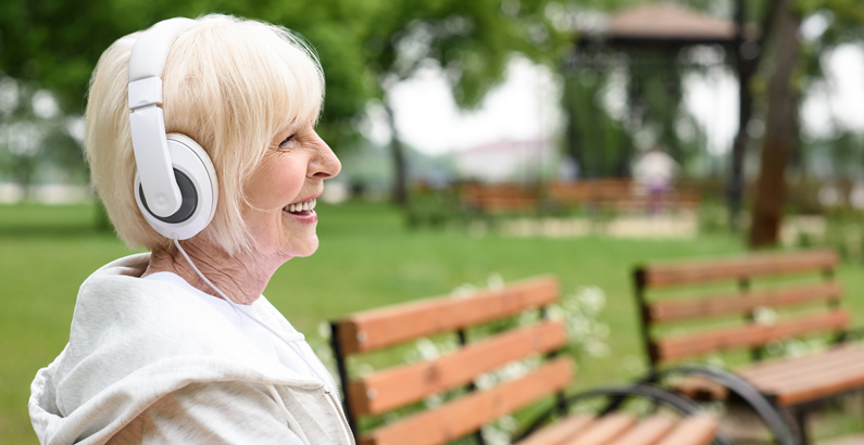 Mulher idosa sentada em um banco ouvindo música com fones de ouvido brancos